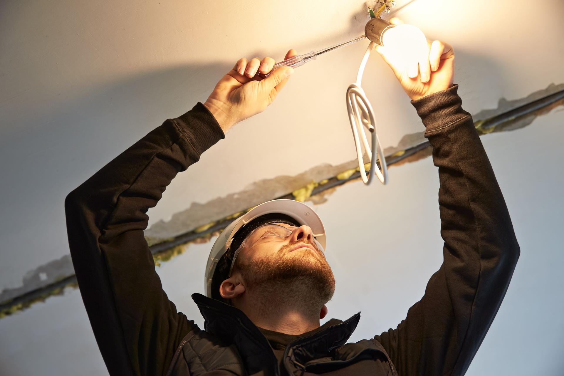 Replacement electrician, focused on wiring a temporary light bulb fixture.